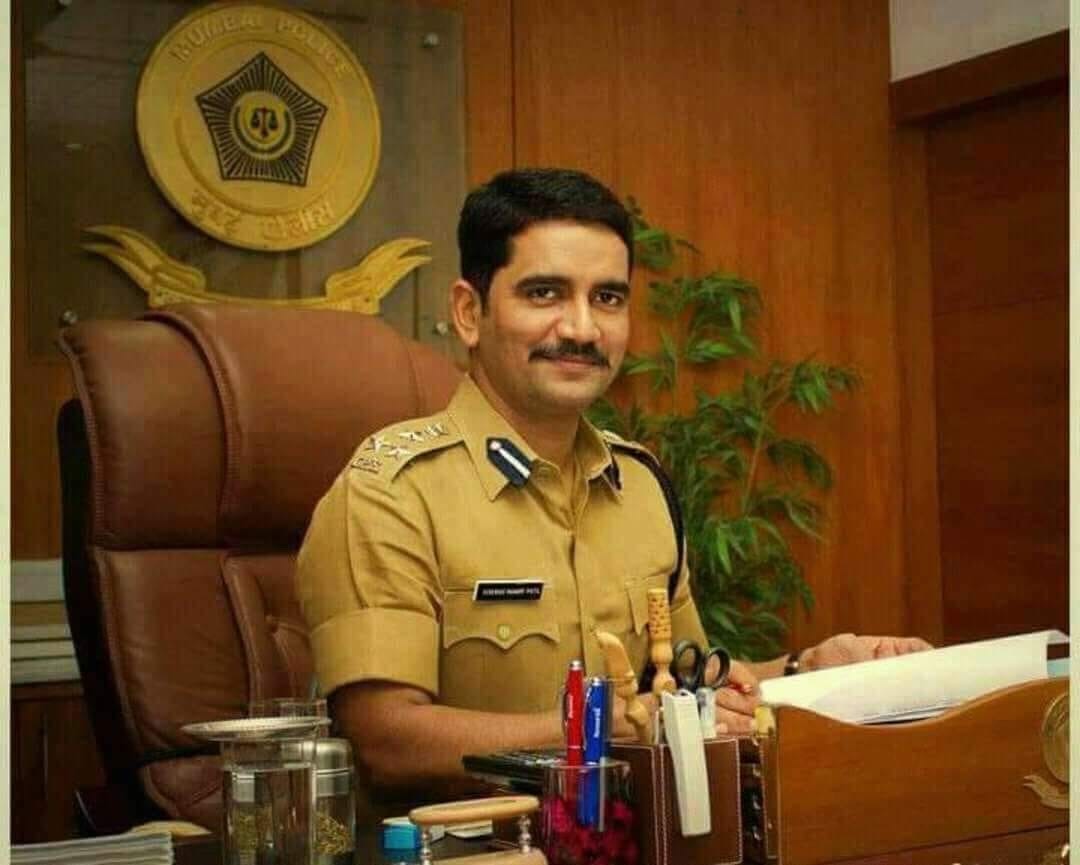 Vishwas Nangre Patil seated at his desk in uniform, with the Mumbai Police emblem on the wall behind